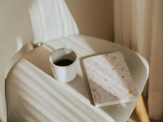 A tea mug amd a journal notebook on a chair with sunlight shadows