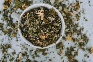 a white cup on a white surface with loose leaf herbal tea