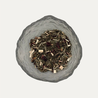 Glass bowl filled with dried herbs and spices on a light grey background