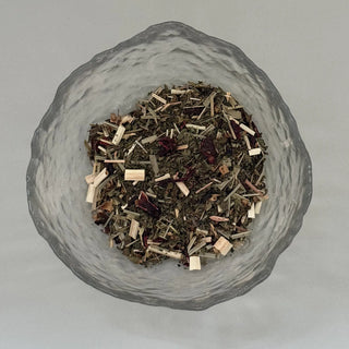 Glass bowl filled with dried herbs and spices on a light grey background