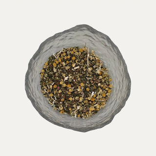 Glass bowl filled with dried herbs on a light grey background