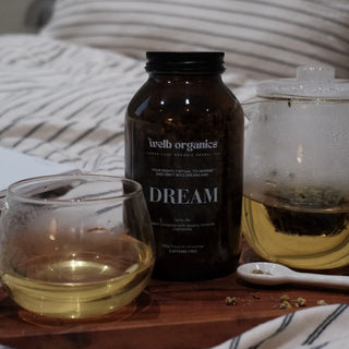 Brown tea jar labeled 'Dream' by welb organics on a wooden tray with a cup and tea pot.