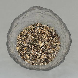 Glass container filled with a mix of dried herbs on a grey background