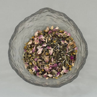 Glass container with dried herbs and flowers on a light grey background