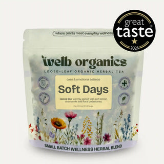 A stand-up pouch of Welb Organics Soft Days loose-leaf herbal tea on a light gray background, with a black circular 'great taste 2026' badge at the top right and a text banner at the top left reading 'Emotional Balance Calm + Mood'. The package is mostly off-white with a cream label, dark green brand text, and multicolored floral illustrations along the bottom.