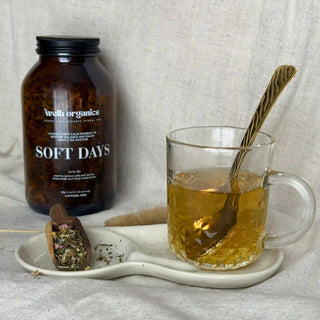 Glass mug with tea and a spoon, next to a bottle labeled 'welb organics' on a textured surface.